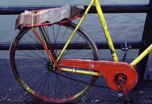 An old, well used red and yellow bike is parked on a canal bridge during a rainy day in Amsterdam, Netherlands.