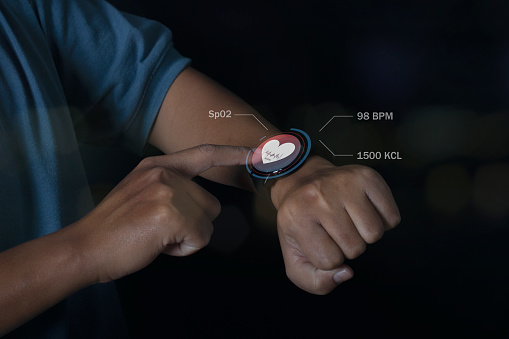 Man using smart watch technology checking heart rate with health app icon on the screen. Holographic icon user interface. Futuristic smart watch technology. Healthcare concept.