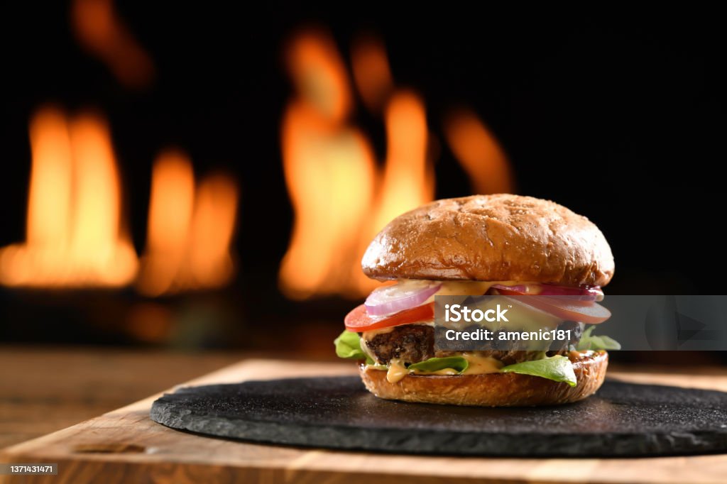 Beef cheeseburger on black plate with flames in background Meat cheeseburger with vegetables on black plate with flaming background. Burger Stock Photo