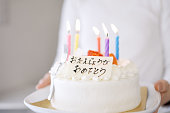 日本語で誕生日おめでとうと言うケーキを運ぶアジアのお母さん
