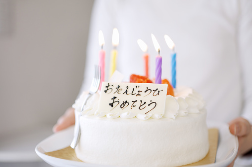 Asian mom carrying a cake that says Happy Birthday in Japanese