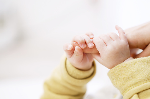 Asian baby holding mom's finger