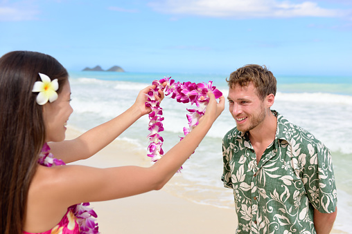 Hawaii woman giving lei garland of pink orchids welcoming tourist on Hawaiian beach. Portrait of a Polynesian culture tradition of giving a flower necklace to a guest as a welcome gesture.
