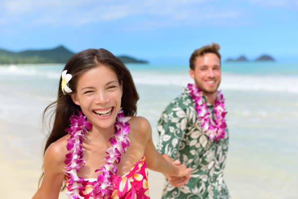 Happy Hawaii beach holiday couple in Hawaiian leis Happy Hawaii beach holiday couple in Aloha shirt and dress and wearing Hawaiian flower leis as a Polynesian culture tradition for welcoming tourists or for a wedding or honeymoon vacation. oahu photos stock pictures, royalty-free photos & images