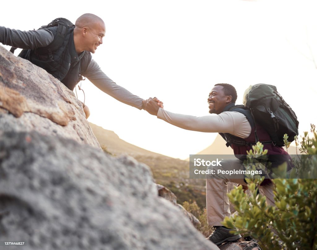 Cropped shot of a handsome young man helping his friend along a mountain during their hike There you go Support Stock Photo