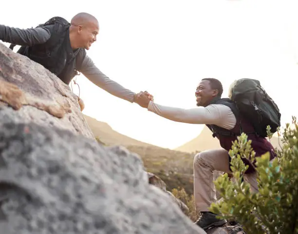 Photo of Cropped shot of a handsome young man helping his friend along a mountain during their hike