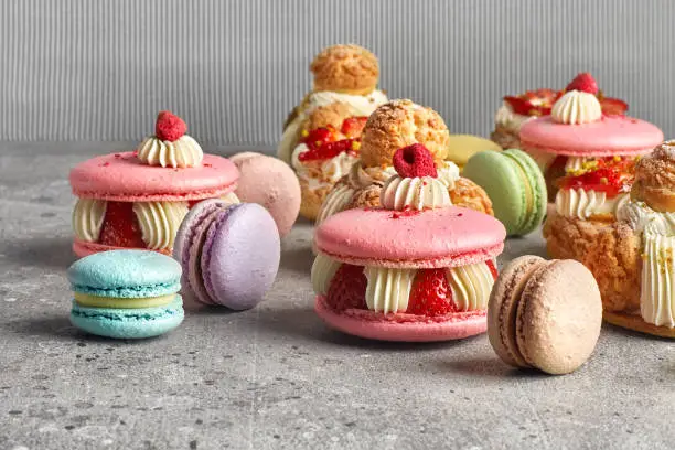 Selection of various pieces of cake - Choux pastries, macarons, chocolate velvet cake on a gray stone background. copy space