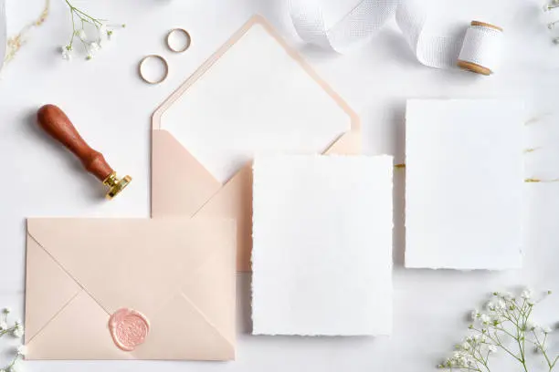 Photo of Wedding stationery set. Flat lay wedding invitations, pastel pink envelopes, wax seal stamp, golden rings, flowers on marble desk.