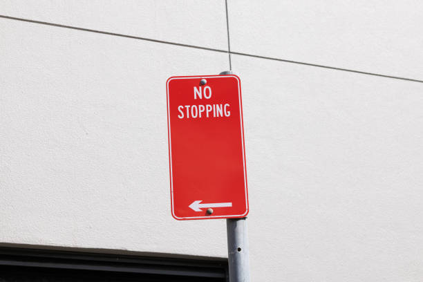Red metal No stopping sign on a gray metal pole, with a wall behind.