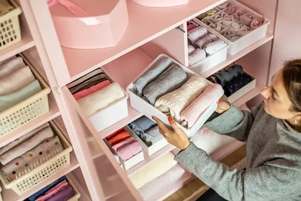 Happy young mother enjoying tidying up at female child wardrobe closet neatly folded clothes in plastic case box for comfortable vertical storage. Modern female cleanup kids cupboard Konmari method