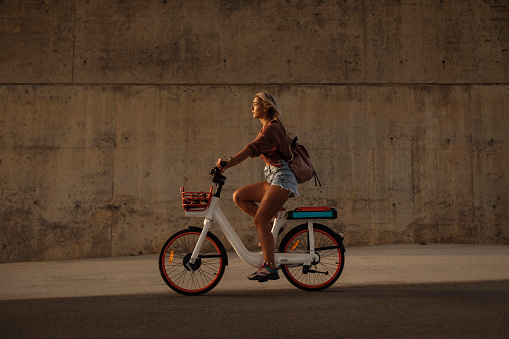 Side shot of a young pretty blond woman riding a city bicycle during sunset