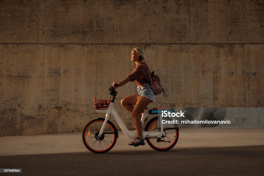Having the time of her life Side shot of a young pretty blond woman riding a city bicycle during sunset Electric Bicycle Stock Photo