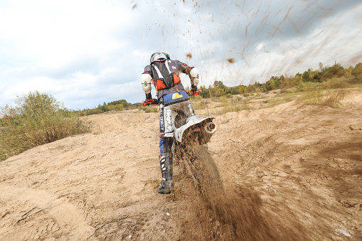 Male portrait of motocross enduro rider outdoors. Sports concept for motorsport on sports track. Professional biker with helmet and stunt motorcycle. Man with protective sportswear. Mud from wheels