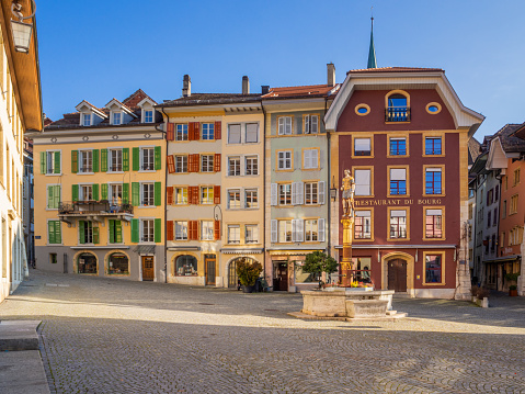 view across the square to the surrounding old and colorful buildings and one of the three historic old town fountains, the Justice Fountain on Burgplatz square. 02/13/2022 - Burggasse, 2502 Biel Bienne, canton Bern, Switzerland