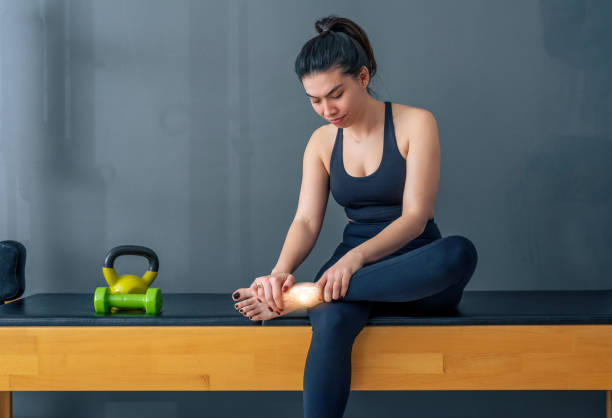 Sporty Woman sitting with injured ankle Sporty Woman sitting with injured ankle JOINT AND MUSCLE PAIN stock pictures, royalty-free photos & images