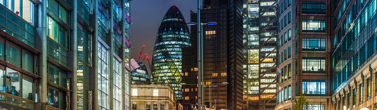 The iconic curves of The Gherkin framed by the illuminated office buildings of the City of London’s Square Mile Financial District, UK.