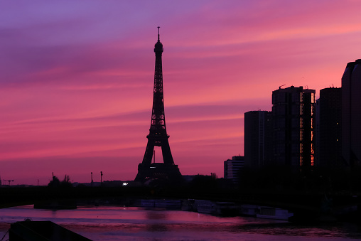 Group of modern buildings in front of the water of Seine river. Dramatic sky with colorful clouds. Silhouette of a cityscape at sunrise with skyscrapers.