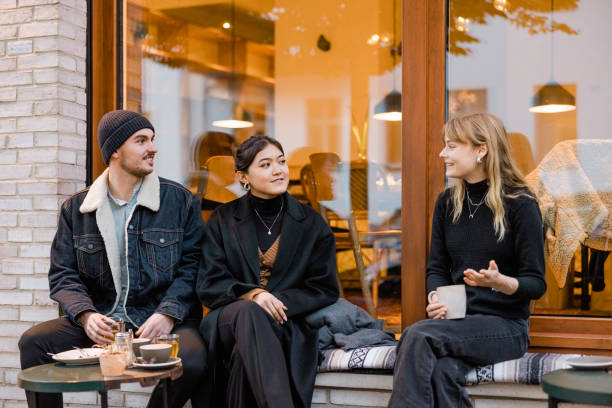 tres amigos sentados en el café de la calle hablando mientras toman café - couple outdoors coffee friendship fotografías e imágenes de stock