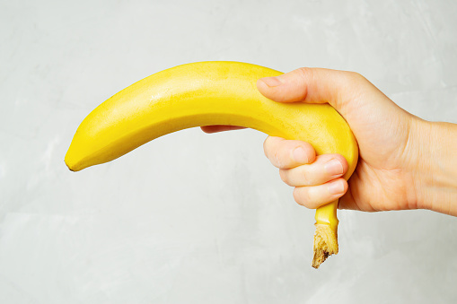 Female hand holding a fresh ripe banana against a neutral background.