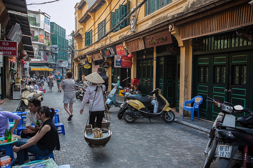 Street trader, tourist, outdoor café,  motorbikes and shops in the Old Quarter of Hanoi, Vietnam