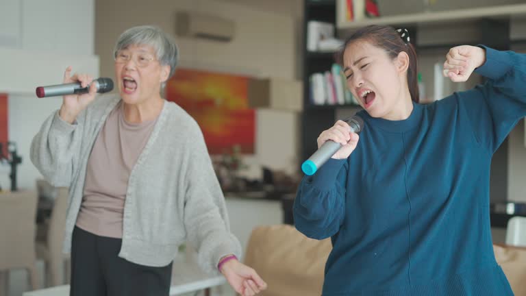 Asian Chinese Senior woman singing karaoke dancing with her daughter in living room during weekend leisure activities