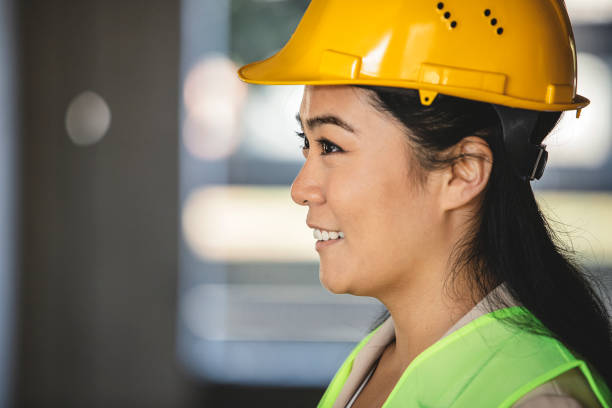 Portrait of successful Asian woman constructor wearing helmet and safety yellow vest at the building site