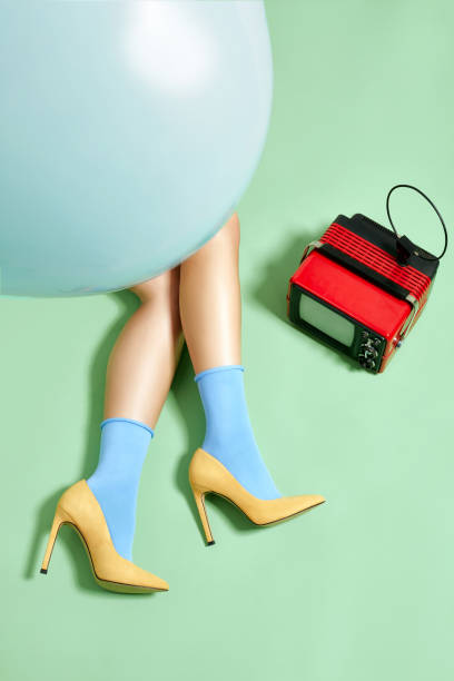 Female legs in socks and high-heeled shoes on studio background with vintage TV Slender legs of young woman hiding under blue balloon in socks and stylish yellow suede high-heeled shoes lying on light green studio background with vintage TV nearby womens blue suede shoes stock pictures, royalty-free photos & images