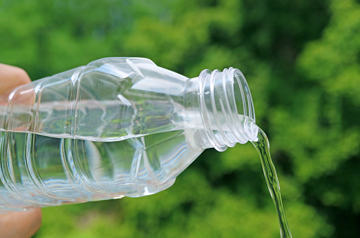 Drinking water being poured from plastic bottle with blurry green foliage in background