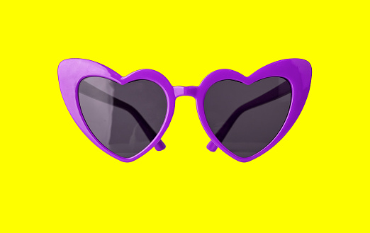 Bright violet heart-formed glasses on yellow background. Valentines day or summer rest concept. High quality photo