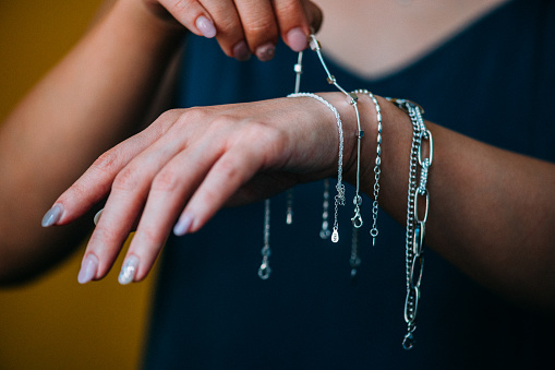 Close-up shot of women's choose silver bracelets on her hands on a yellow background. Entrepreneur's hand arranging the jewels to get the product ready and send it to her client .