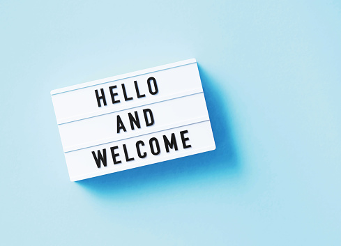 Hello and welcome written white lightbox sitting on blue background. Horizontal composition with copy space.