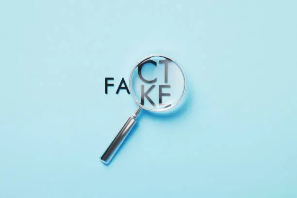 Photo of Magnifier Over Fact Or Fake Words On Blue Background