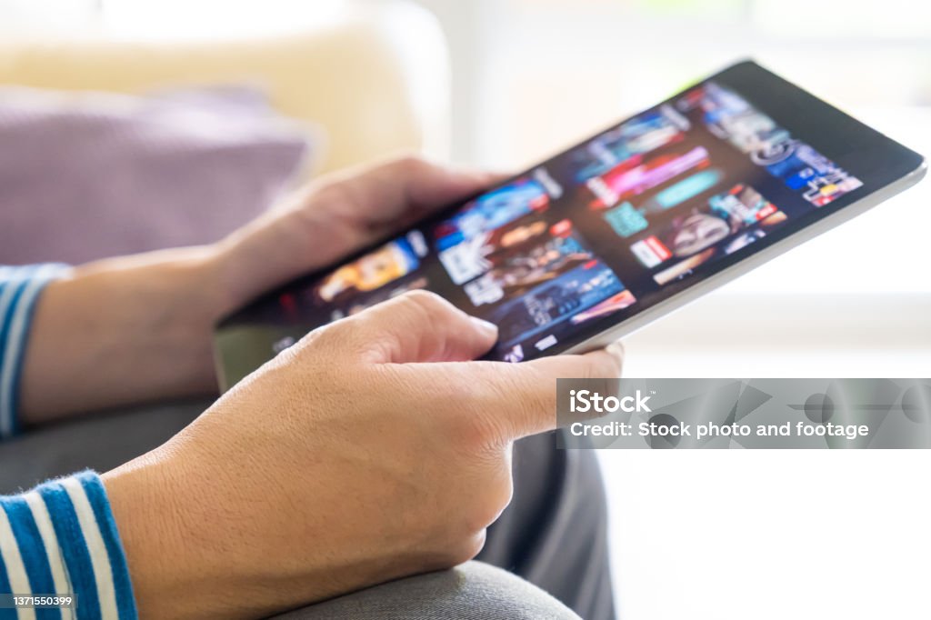 Selective focus at men hand and digital tablet. Young Adult Asian man holding tablet device while choose online movie streaming application with mobile wireless network at home. Entertainment concept. Streaming Service Stock Photo