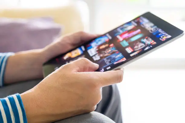 Photo of Selective focus at men hand and digital tablet. Young Adult Asian man holding tablet device while choose online movie streaming application with mobile wireless network at home. Entertainment concept.