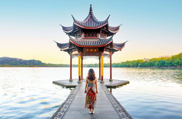 beau paysage au lac de l’ouest de hangzhou, une femme élégante en robe regarde dans le pavillon jixian au lever du soleil - ancient architecture asia asian culture photos et images de collection