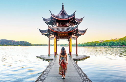 Beautiful scenery at Hangzhou West Lake, beautiful and elegant woman in dress looks on into the Jixian Pavilion and the vast lake at sunrise, Chinese characters translate as ‘Jixian Pavilion'