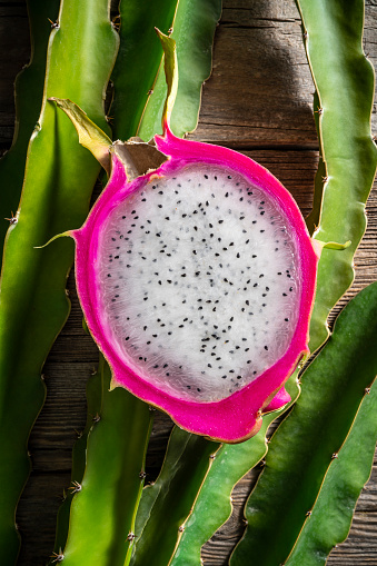 Half pink Pitahaya Dragonfruit fruit cut with white meat on a rustic wooden table board with pitaya plants