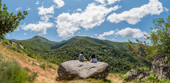 Lugo, Galicia, Spain - August 8 2021: Couple with their backs to nature sitting on a huge rock
