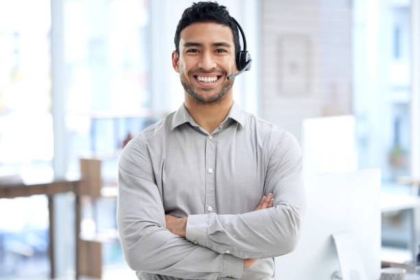 retrato de un joven hombre de negocios usando un auricular en una oficina moderna - agente de servicio al cliente fotografías e imágenes de stock
