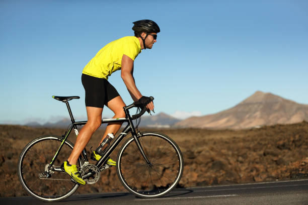 Biking cyclist male athlete going uphill on open road training hard on bicycle outdoors at sunset. Nature landscape. stock photo