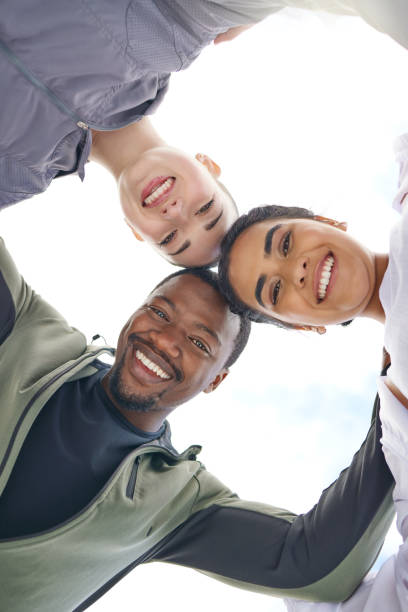 low angle shot of a group of sporty young people joining their heads together in a huddle outdoors - exercising motivation looking up african descent imagens e fotografias de stock