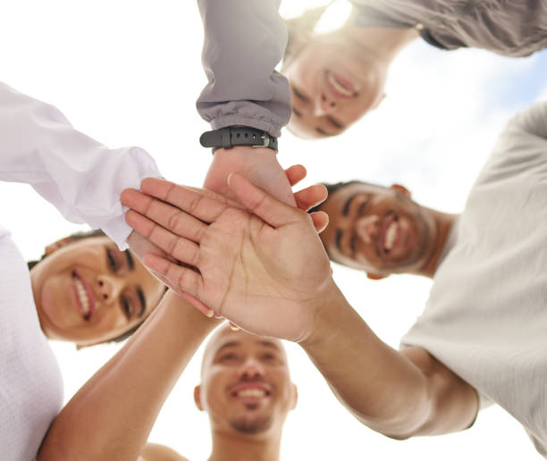 low angle shot of a group of sporty young people joining their hands together in a huddle - exercising motivation looking up african descent imagens e fotografias de stock