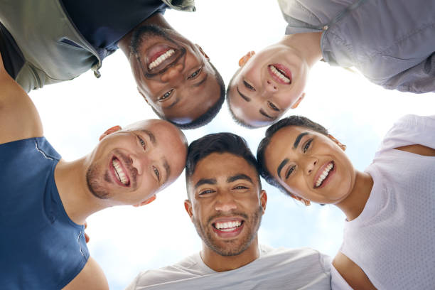 low angle shot of a group of sporty young people joining their heads together in a huddle outdoors - exercising motivation looking up african descent imagens e fotografias de stock