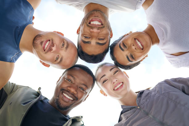 low angle shot of a group of sporty young people joining their heads together in a huddle outdoors - exercising motivation looking up african descent imagens e fotografias de stock