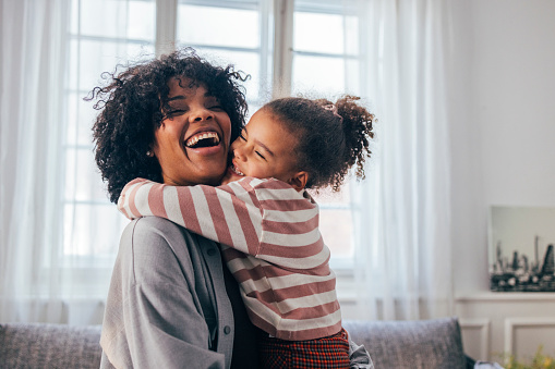 Una feliz mujer afroamericana siendo abrazada por su linda hija pequeña en casa photo
