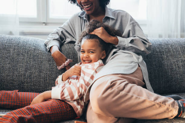 istock A Cute African-American Child Looking At Camera While Sitting On The  Sofa With Her Unrecognizable Mother And Smiling 1371563908