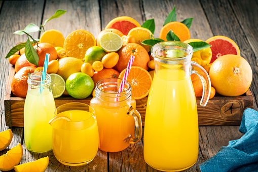 Assorted citrus fruits juice as Orange juice, lemonande and mandarine juice on rustic wood table background with assorted citrus fruits in a wood crate tray