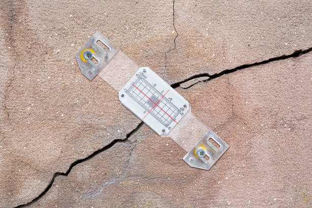 Deep crack in a damaged old plaster wall cause due to subsidence of foundations structural failures with plastic mechanical crack meter designed to measure movement across surface cracks and joints la grieta profunda en una pared de yeso vieja dañada causa debido al hundimiento de los cimientos fallas estructurales con medidor de grietas mecánicas de plástico diseñado para medir el movimiento a través de grietas y juntas superficiales