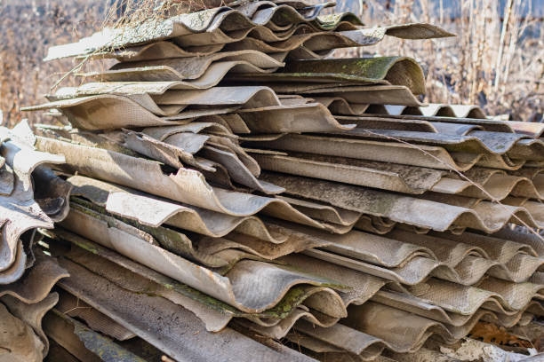 Broken pieces of slate, taken from the roof, are collected in a large high stack in the garden among dry grass, in the warm sun, a pile of building materials stock photo