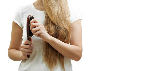 A girl with long blonde hair holds a comb and hair loss in her hands. The problem of alopecia. High quality photo